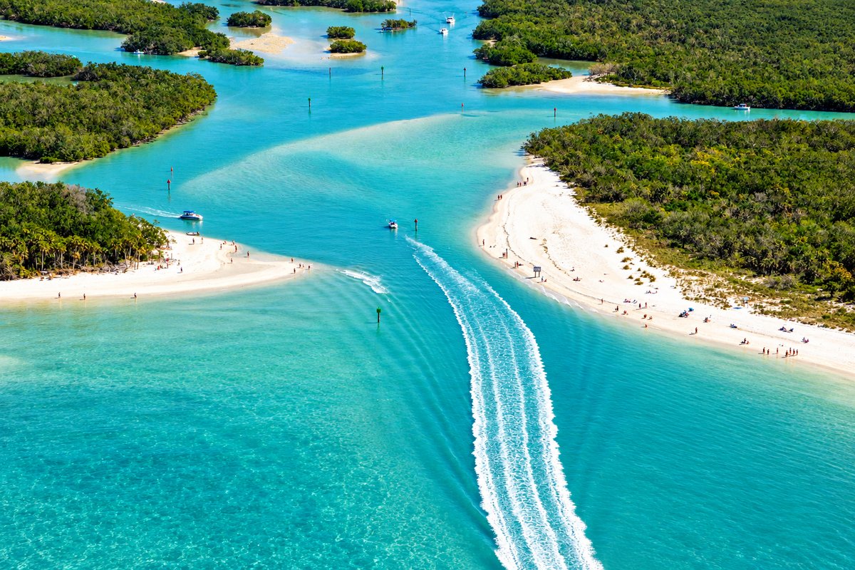 Aerial view of a boat leaving a white wake through a marked channel between mangrove islands and white sand beaches in Southwest Florida